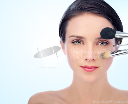 Image of Portrait, beauty and makeup brushes with natural woman in studio on blue background for cosmetology. Face, skincare or cosmetics and confident young model with product for foundation application