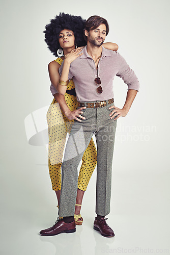 Image of Couple, portrait and fashion in confidence for style, outfit or clothing on a gray studio background. Young interracial man and woman in stylish retro or vintage pants, shirt or jumpsuit with jewelry