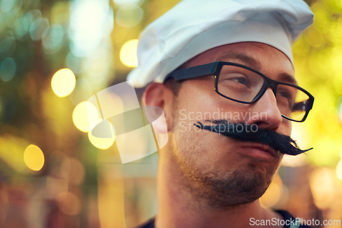 Image of Man, fake mustache and beret in chef costume with comic face, creative and confident in french baking. Young person, glasses and cooking job in bokeh and culinary education in pastry art in europe