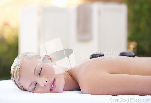 Image of Spa, woman and hot stone on massage bed with peace for wellness, zen and beauty treatment for body care. Person, relax and stress relief at resort, salon table and luxury on holiday or vacation