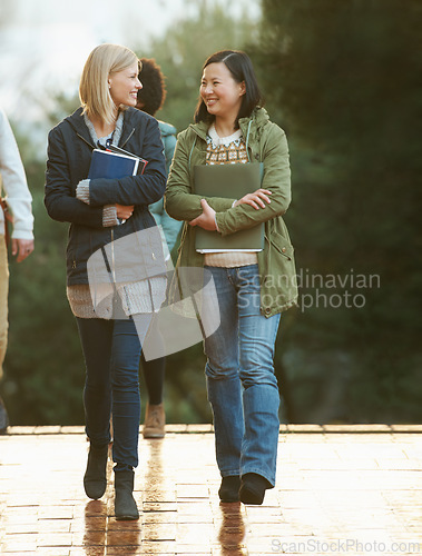 Image of Students, women and friends on campus for college, conversation while walking to class and smile. University, communication and books for studying, education and academic growth with talk outdoor