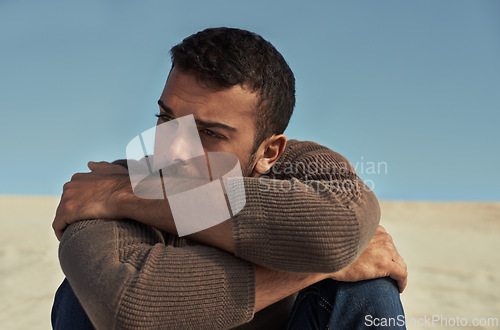 Image of Depressed, model or man in the desert thinking of travel in summer sitting on holiday vacation. Upset, worry or stress with face of nervous person on the ground or sand dunes with anxiety or fear