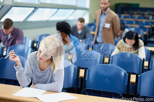 Image of Exam, classroom and student with pen for thinking, assessment and writing at campus. Woman, planning and sitting with paper for brainstorming, education and growth of knowledge in university class