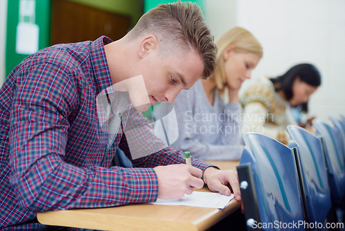 Image of University student, desk and writing exam in classroom for education assessment for knowledge, diploma or scholarship. Men, woman and test in London lecture hall or study document, academy or college