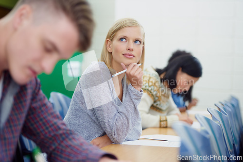 Image of Student, thinking and exam writing in university classroom for education assessment for learning, answer or scholarship. Female person, pencil and thoughts in lecture hall or idea, school or London