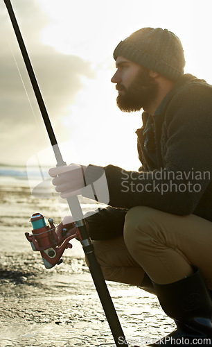 Image of Beach, ocean and man with fishing rod in water in the morning in summer outdoor for hobby or leisure. Sea, fisherman and person with pole in nature, serious or angler thinking of recreation with reel