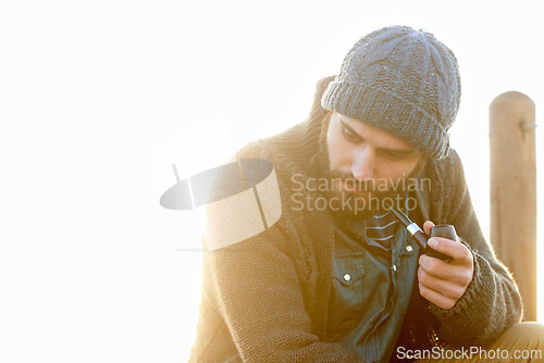 Image of Young, man and smoking a pipe in outdoor, thinking and tobacco habit in morning by sunrise. English guy, nicotine addiction and retro smoker for calm, satisfaction and vacation by ocean in cape town