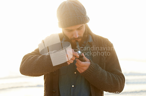 Image of Smoker, man and lighting a pipe in outdoor, relax and sailor habit on winter morning in sunrise. English guy, nicotine addiction or vintage smoking for flavor, taste or vacation by ocean in cape town