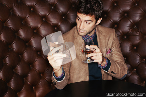 Image of Cigar, businessman and drinking whiskey at club, fashion and person in a suit with alcohol at vintage bar. Mafia, smoking and serious person with scotch, beverage or brandy in glass for luxury at pub