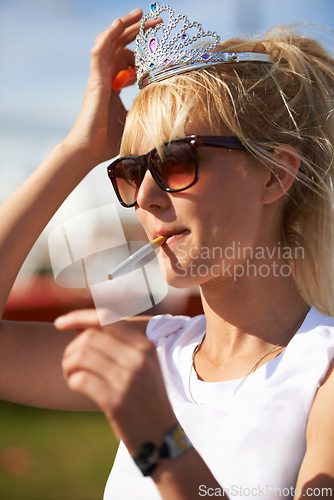 Image of Crown, smoking and young woman with cigarette in nature at outdoor festival, event or party. Fun, tiara and female person with tobacco, sunglasses and casual fashion in outside park or field.