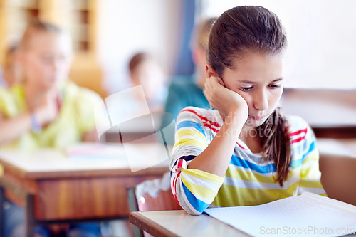 Image of Child, school and desk with book or bored in classroom or education lesson or reading, knowledge or studying. Girl, kids and unhappy or learning or tired pupil with paper or fatigue, student or moody