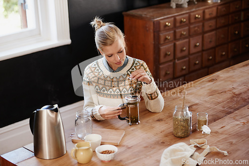 Image of Woman, herbal tea and prepare with leaves at kitchen table with french press or kettle for health, beverage or detox. Female person, plunger and relax morning for breakfast drink, vacation or home