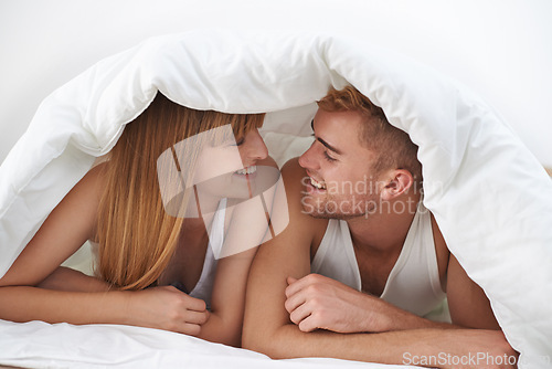 Image of Happy couple, romantic and moment in bed, together and excited for marriage, happy and relax. Partners, speaking and smile with love, home and lying under duvet for bonding in morning at apartment