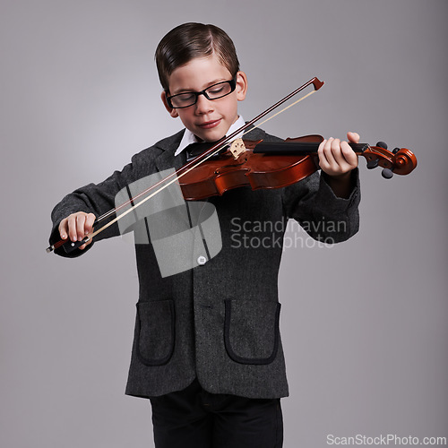 Image of Smile, music and kid with violin in studio for practice with suit and glasses for fashion. Happy, style and cute young boy child playing string instrument with spectacles by gray background.