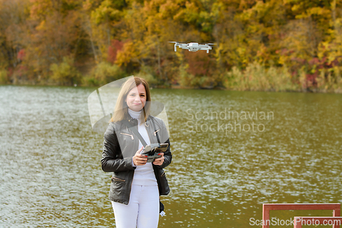 Image of A young beautiful girl launches a radio-controlled quadcopter on the shore of an autumn lake, the girl looks into the frame