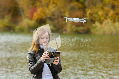 Image of A young beautiful girl launches a radio-controlled quadcopter on the shore of an autumn lake, the girl adjusts the camera