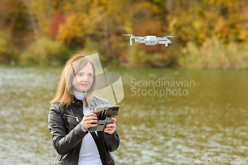 Image of A young beautiful girl launches a radio-controlled quadcopter on the shore of an autumn lake, the girl looks at the quadcopter