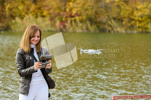 Image of A young beautiful girl launches a radio-controlled quadcopter on the shore of an autumn lake