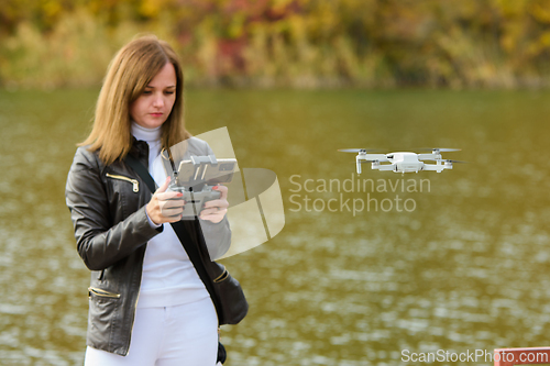 Image of A young beautiful girl launches a radio-controlled quadcopter on the shore of an autumn lake