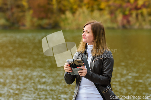 Image of A young beautiful girl launches a radio-controlled quadcopter on the shore of an autumn lake, the girl looks at the drone