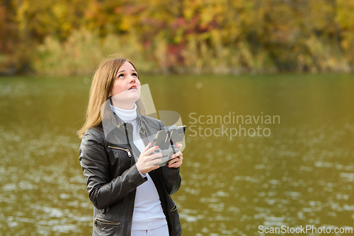 Image of A young beautiful girl launches a radio-controlled quadcopter on the shore of an autumn lake, the girl looks above herself in search of a drone
