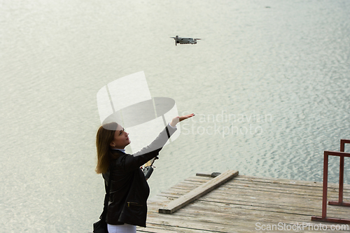 Image of A young beautiful girl launches a radio-controlled quadcopter on the shore of a lake, the girl extended her hand to the drone