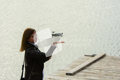 Image of A young beautiful girl launches a radio-controlled quadcopter on the shore of a lake, the drone lands on the girl's hand