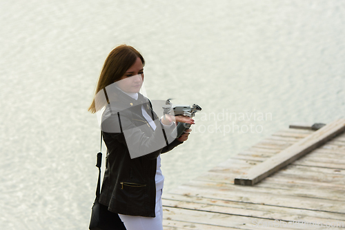 Image of A young beautiful girl launches a radio-controlled quadcopter on the shore of a lake, the drone landed on the girl's hand, the girl looks at it