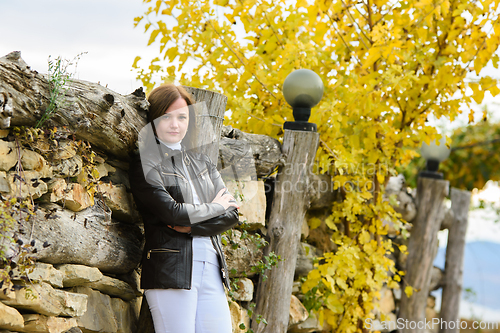 Image of Young beautiful girl in casual clothes against the background of an old fence and autumn yellow foliage