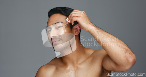 Image of Man, face and essential oil for beauty, skincare and cosmetics product on a gray, studio background. Young asian person in portrait with facial serum, dermatology dropper or collagen for skin care