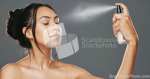 Image of Face, woman and spray after makeup studio with product for mockup in cosmetics on gray background. Female model, happy and smile for beauty, application and facial mist on skin, hydration and glow