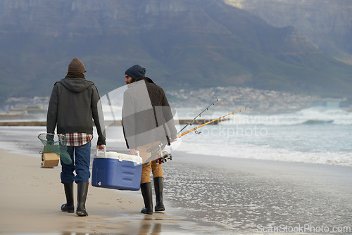 Image of Ocean, fishing and men walking together with cooler, tackle box and holiday conversation from back. Beach, fisherman and friends with rods, bait and tools at waves on winter morning vacation at sea.