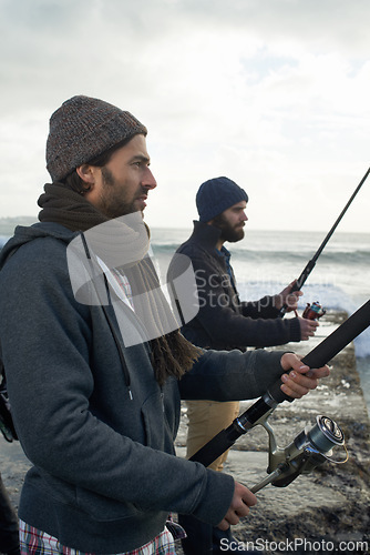 Image of People, fishing and friends on trip at beach, relaxing and casting a line by ocean waves. Men, fisherman and cloudy sky on vacation or holiday, hobby and bonding by water and support on adventure