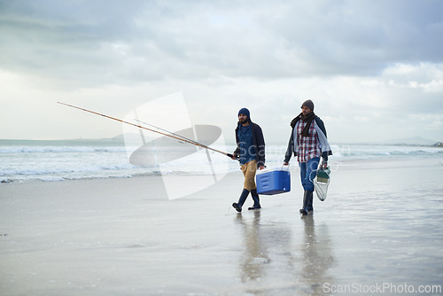 Image of Winter, fishing and men walking on beach together with cooler, tackle box and holiday conversation. Ocean, fisherman or friends with rods, bait and tools in nature on morning vacation with cloudy sky