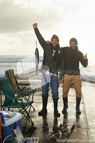 Image of Happy, portrait and men fishing at beach with pride for tuna catch on ocean pier at sunset. Fisherman, friends and smile holding fish in hand in nature at sea on holiday, adventure or vacation