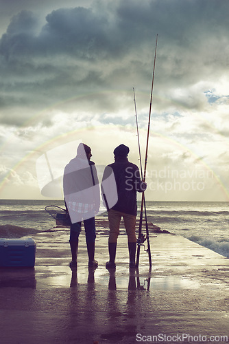 Image of Back, pier and beach with fishermen, sunset or hobby with equipment or weekend break. People, ocean or friends with tools for activity or early morning with waves, shore or seaside with conversation