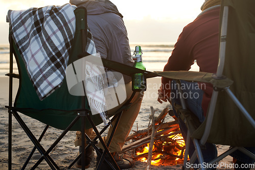 Image of Beer, beach and man friends by fire on sand by ocean or sea together for travel, holiday or vacation. Nature, relax and people drinking on coast from back with view of sunset, horizon and coast