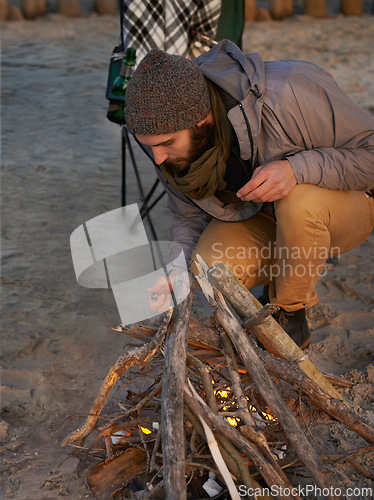 Image of Campfire, nature and man by beach for travel on vacation, adventure or holiday camping. Wood, outdoor and young male person sitting on chair in sand with flame for heat on weekend trip in winter.