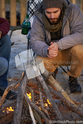 Image of Campfire, wood and men by beach for travel on vacation, adventure or holiday camping. Nature, outdoor and young male people sitting on chair in sand with flame for heat on weekend trip in winter.
