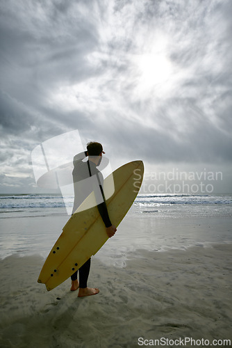 Image of Man, surfboard and adventure at beach on vacation, weekend and sports for fitness in water. Male person, back and cloudy sky for ocean waves, wetsuit and traveling on holiday or getaway for peace