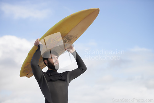 Image of Man, surfboard and adventure at beach on holiday, weekend and sports for fitness in water. Male person, balance and cloudy sky on tropical island, wetsuit and travel on vacation or getaway for peace