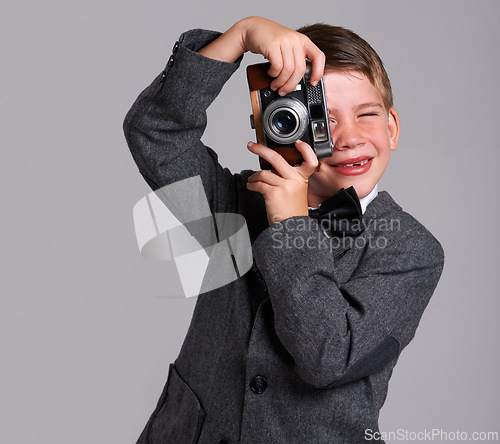 Image of Camera, photography and boy child in studio in elegant, classy or fancy suit outfit with smile. Happy, vintage and young kid with dslr equipment for picture with bowtie for fashion by gray background