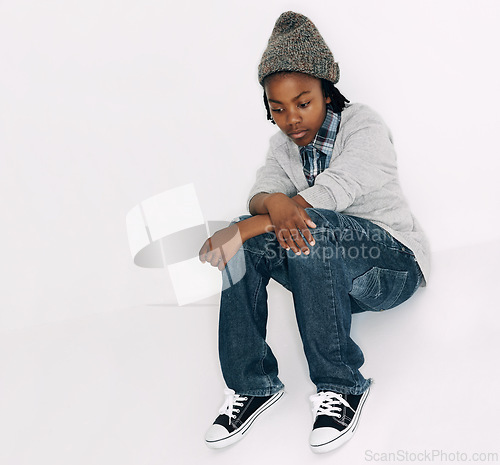 Image of Child, sad and fashion with problem and frustrated with depression in a studio. Youth, annoyed and bored African male boy with casual fashion and gen z clothes sitting with white background and issue