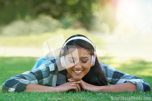 Image of Woman, headphones and streaming song on grass, peace and calming podcast in outdoors. Female person, happy and relaxing on lawn, weekend playlist and subscription for audio or sound on vacation