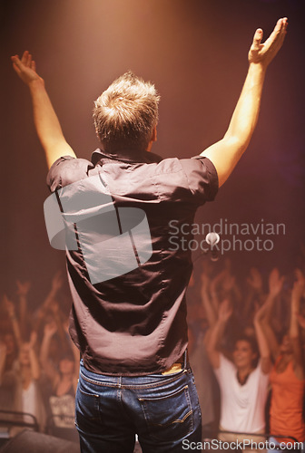 Image of Man, stage and audience for motivation, inspiration and coaching with spotlight, arms or mic in USA. Male coach, motivational and speaker with hands raised before crowd of people cheering and smiling