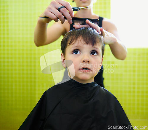 Image of Child, boy and barber with haircut at salon for grooming, hairstyle or serious with scissors. Hairdresser, person or kid for hair treatment, haircare and hairdressing with comb, confidence or looking