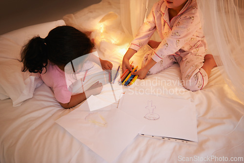 Image of Girls, color pencil and drawing on bed for sleepover, creative and relax in bedroom for weekend. Young kids, playing or educational toys at night in pajamas, friends or bonding by fairy light in home