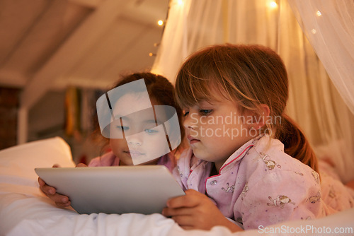 Image of Girls, tablet or games on bed at night, playing or digital technology for cartoons with love in home. Young kids, friends or connection by fairy light, tent or streaming video for bonding together