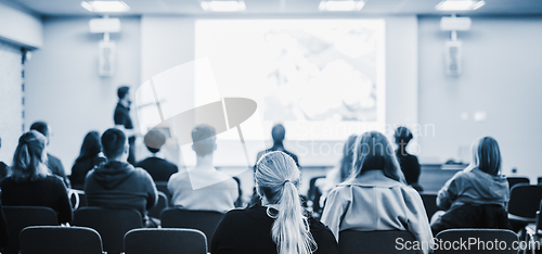 Image of Speaker giving a talk in conference hall at business event. Rear view of unrecognizable people in audience at the conference hall. Business and entrepreneurship concept. Blue tones black and white.