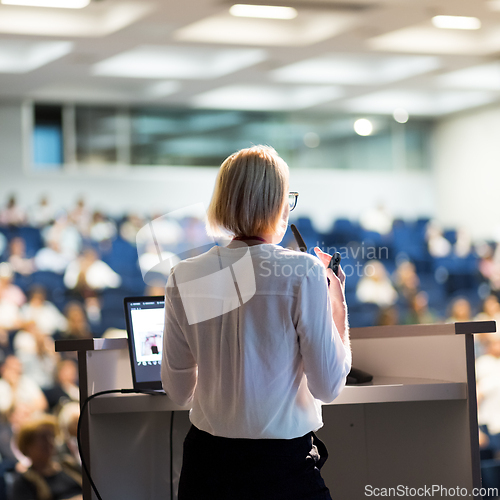 Image of Female speaker giving a talk on corporate business conference. Unrecognizable people in audience at conference hall. Business and Entrepreneurship event.